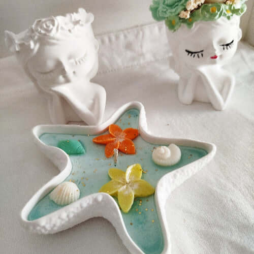 Bougie parfumée en étoile avec support minéral, fleurs orange et jaune, coquillages et paillettes dorées.