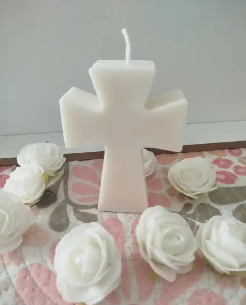 Bougie artisanale en forme de croix blanche entourée de fleurs blanches