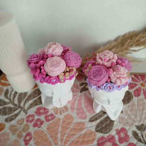 Bougie décorative sur support minéral représentant un visage aux yeux fermés avec une couronne florale en cire rose vif.