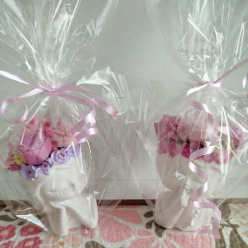 Bougie artisanale sur support en forme de tête pensive, ornée de fleurs en cire dans des tons roses et parme.