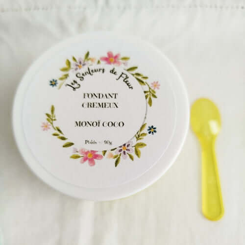 Fondant Crémeux Monoï Coco dans un pot décoré avec une cuillère jaune à proximité.