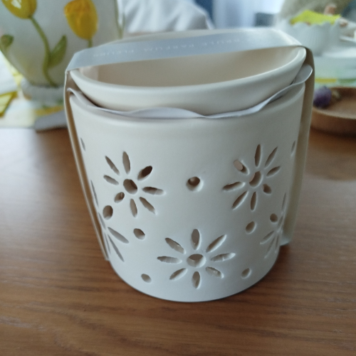 Brûleur à fondants parfumés en céramique blanche avec motif floral ajouré, vu de face sur une table en bois.