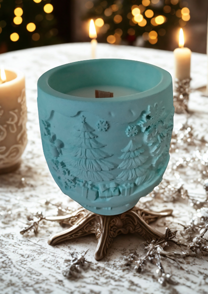 Bougie parfumé Forêt Enchantée en céramique turquoise, décorée de motifs de sapins, sur une table de fête.