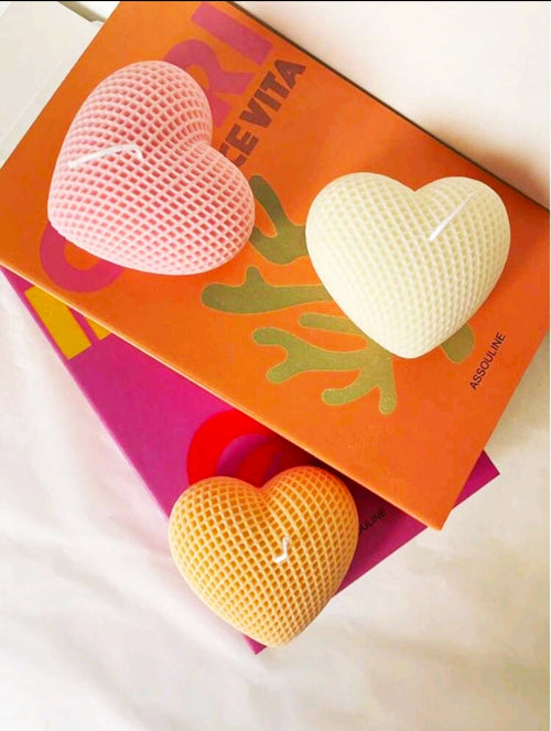 Bougie cœur texturé en couleurs rose, blanc et orange sur des livres colorés.