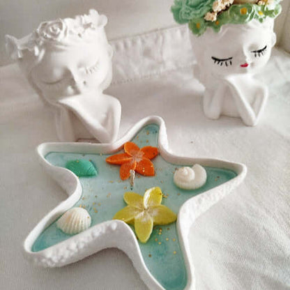 Bougie parfumée en étoile avec support minéral, fleurs orange et jaune, coquillages et paillettes dorées.