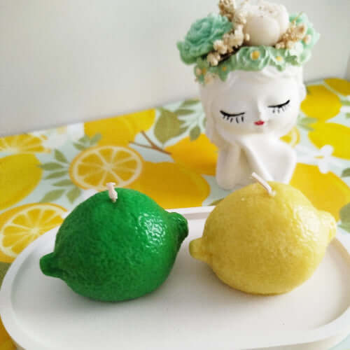 Bougie artisanale verte en forme de citron vert posée sur un plateau blanc.