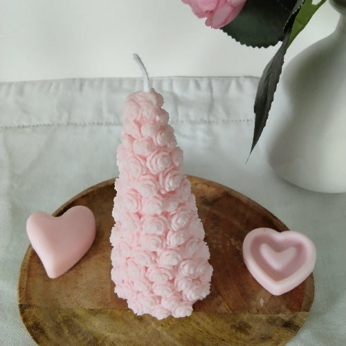 Bougie artisanale avec relief de roses, posée sur un plateau en bois, accompagnée de cœurs fondants.