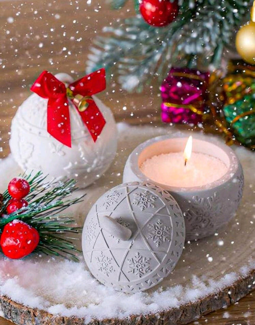Bougie parfumée Flocon d’Hiver sur une table en bois décorée pour les fêtes avec des boules et des branches de sapin.
