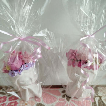 Bougie artisanale sur support en forme de tête pensive, ornée de fleurs en cire dans des tons roses et parme.