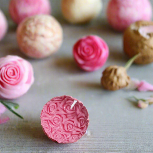 Bougie artisanale en forme de boule ornée de motifs de roses, posée sur une surface scintillante, idéale pour une décoration romantique.

