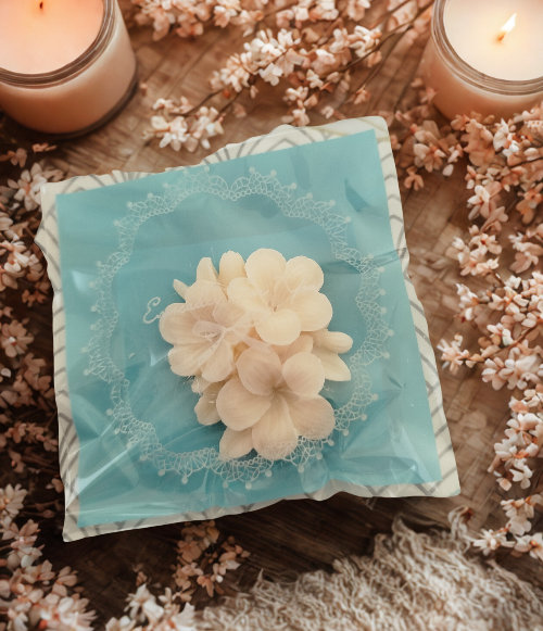 LOT DE 10 FONDANTS PARFUMES AUX SENTEURS VARIEES présenté avec des fleurs et des bougies décoratives.