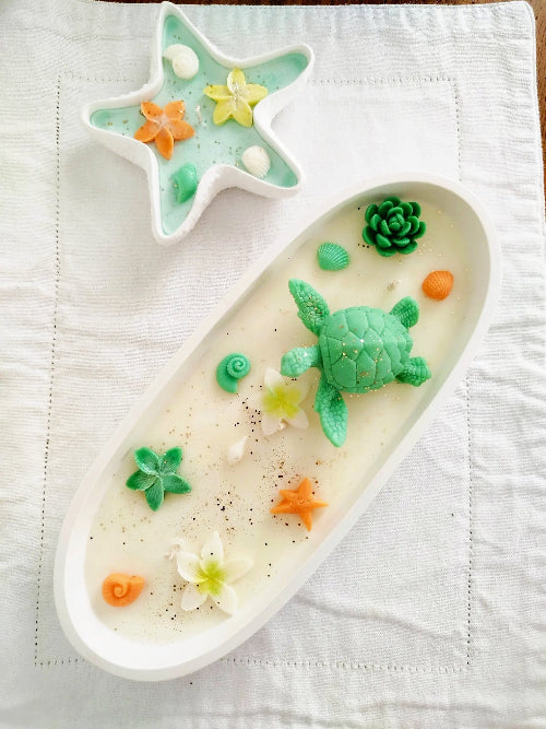 Bougie artisanale parfum monoï décorée avec tortue, fleurs et coquillages dans un contenant minéral fait main.